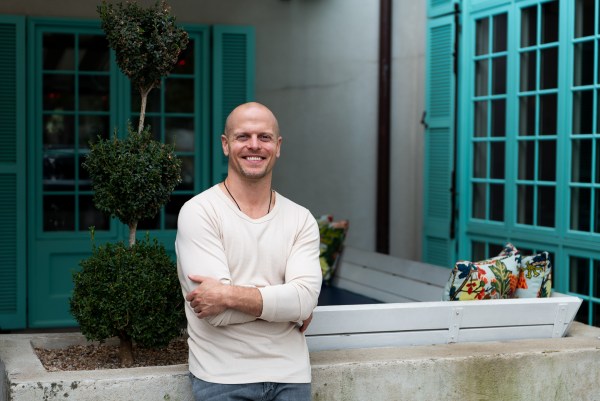 Tim Ferriss smiling near an outdoor patio with aqua shutters.